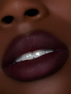 Labios con labial mate color vino oscuro sobre piel morena; los labios están entreabiertos, mostrando parcialmente dientes blancos.