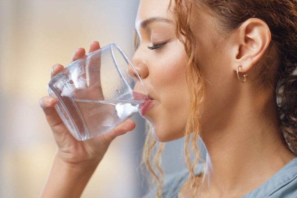 Mujer joven bebiendo un vaso de agua, hidratación saludable para el cuidado de la piel y el bienestar.