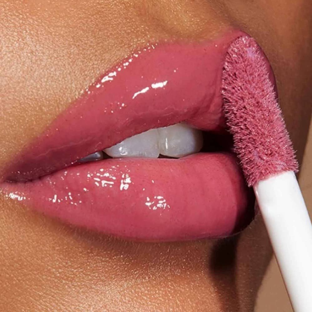 Aplicación de gloss rosado brillante en labios de piel morena, maquillaje hidratante y luminoso con efecto volumen.