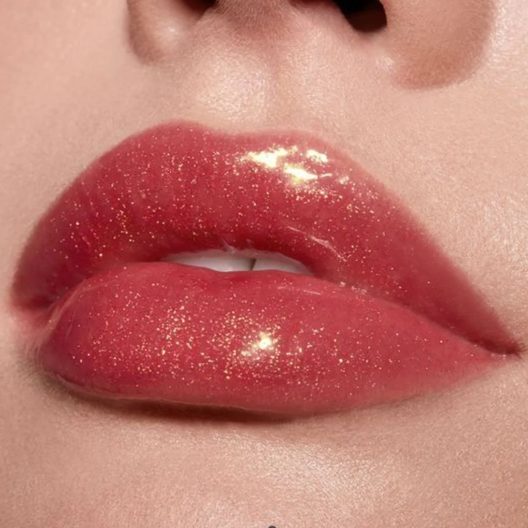 Labios maquillados con brillo labial rosado con destellos dorados, maquillaje luminoso y glamuroso.