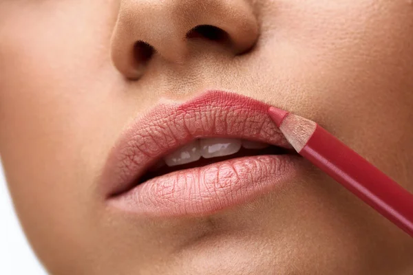 Mujer delineando sus labios con lápiz rojo, técnica de maquillaje para definir el contorno labial.