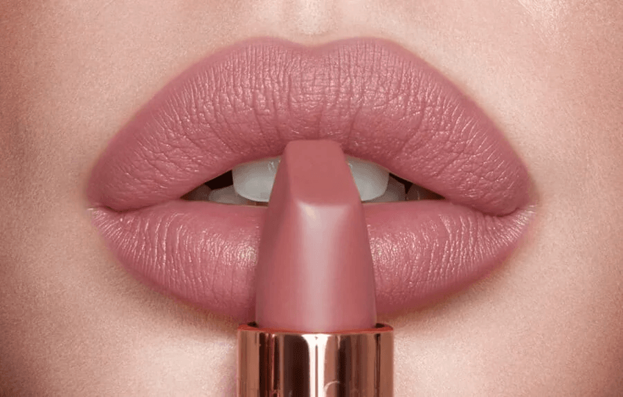 Primer plano de unos labios perfectamente maquillados con labial mate en tono nude rosado. La textura del labial es cremosa y de acabado aterciopelado, resaltando la forma natural de los labios. La barra de labios, en color rosa palo, se aplica cuidadosamente para un look sofisticado y elegante. Imagen ideal para contenidos sobre maquillaje de labios, tendencias de belleza, labiales nude, maquillaje profesional y tips para labios perfectos.