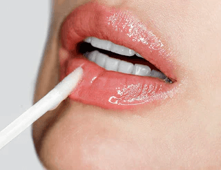 Aplicación de brillo labial rosado sobre labios claros, maquillaje natural y luminoso para un look fresco.