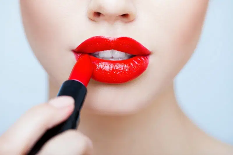Mujer aplicando labial rojo intenso con acabado brillante, dando unos labios definidos y sensuales.