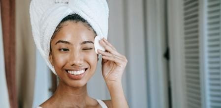 Mujer sonriente sosteniendo una toalla en su rostro, aplicándose una rutina de cuidado de la piel, rutina facial de skincare, productos desmaquillantes