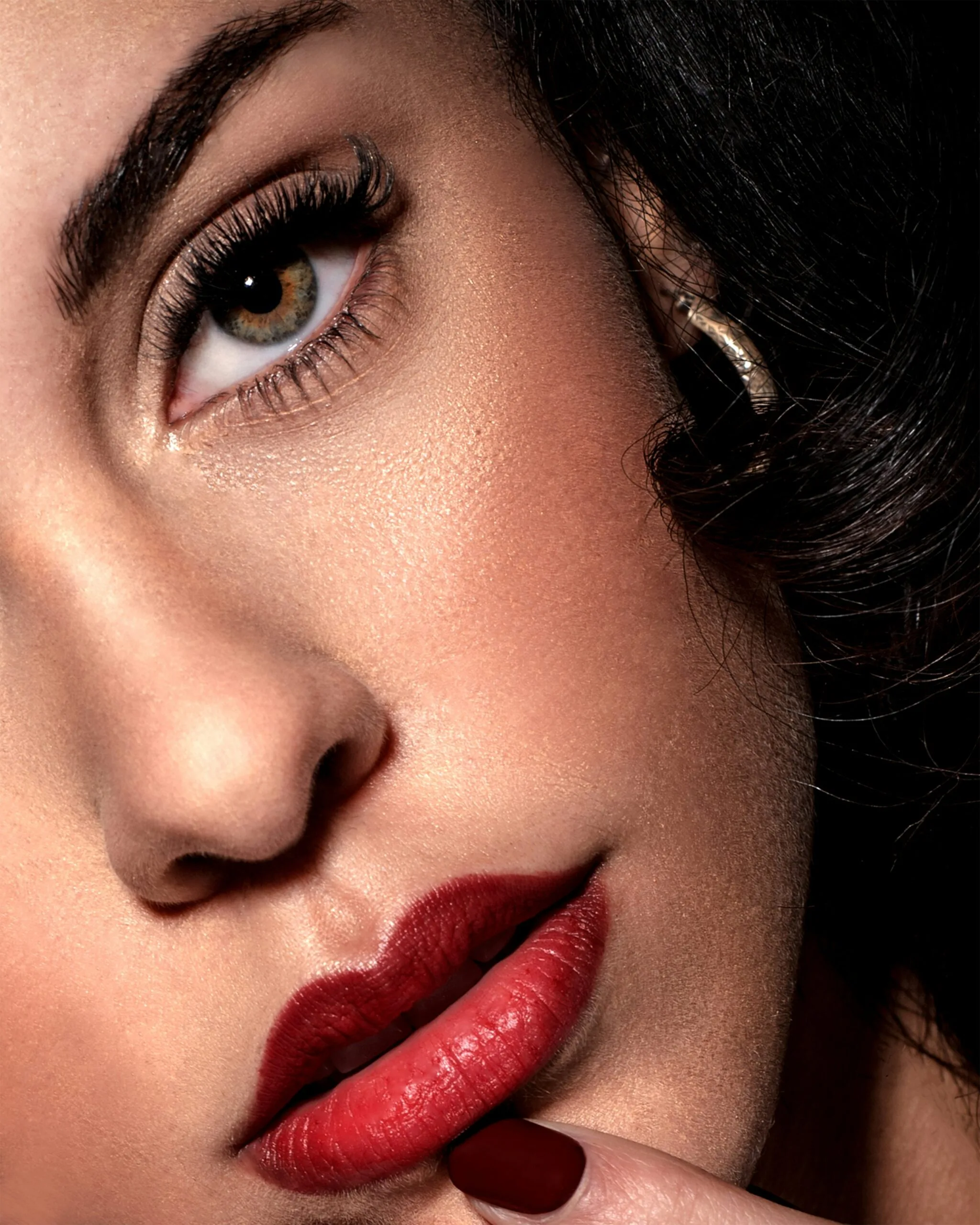 Maquillaje profesional para rostro. La imagen muestra una mujer con piel perfectamente maquillada, destacando un acabado luminoso y natural. Sus labios rojos intensos están delineados con precisión, mostrando un labial de larga duración. El maquillaje de ojos incluye pestañas voluminosas, cejas bien definidas y sombras neutras que realzan la mirada. El acabado de la piel refleja el uso de base de maquillaje de alta cobertura, iluminador facial y rubor sutil. Ideal para inspirar un look elegante y sofisticado, técnicas de maquillaje para resaltar tus rasgos.