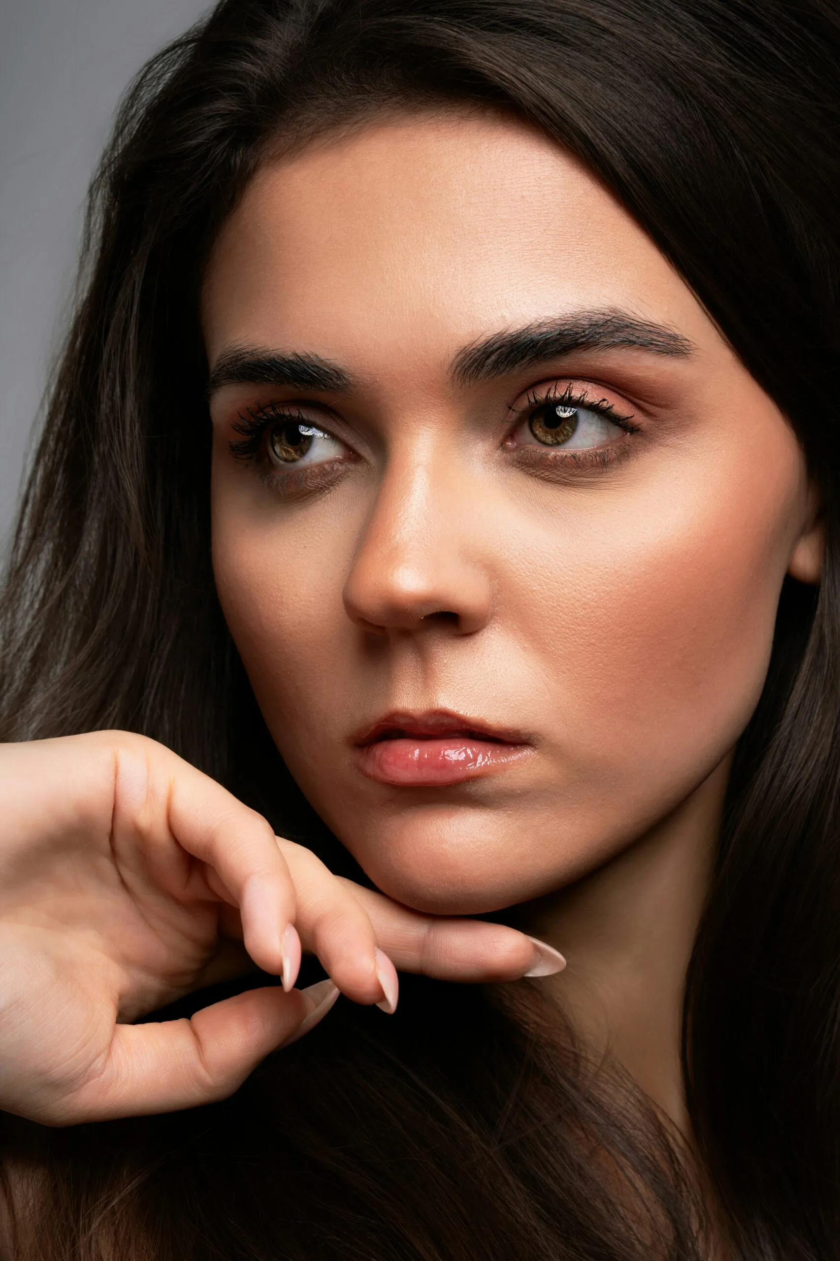 Maquillaje natural profesional. La imagen muestra a una mujer con una piel impecable, resaltando un maquillaje suave y elegante. Sus labios están maquillados con un brillo labial rosado, aportando un efecto fresco y jugoso. Los ojos destacan con una sombra de ojos en tonos cálidos y pestañas definidas, logrando una mirada expresiva y natural. Sus cejas están bien perfiladas y su piel luce con un acabado luminoso, probablemente gracias al uso de base de maquillaje ligera, corrector e iluminador facial. El peinado es suelto y liso, en armonía con el estilo del maquillaje. tipo de rostro, como conocer tu tipo de rostro y lograr el maquillaje perfecto.