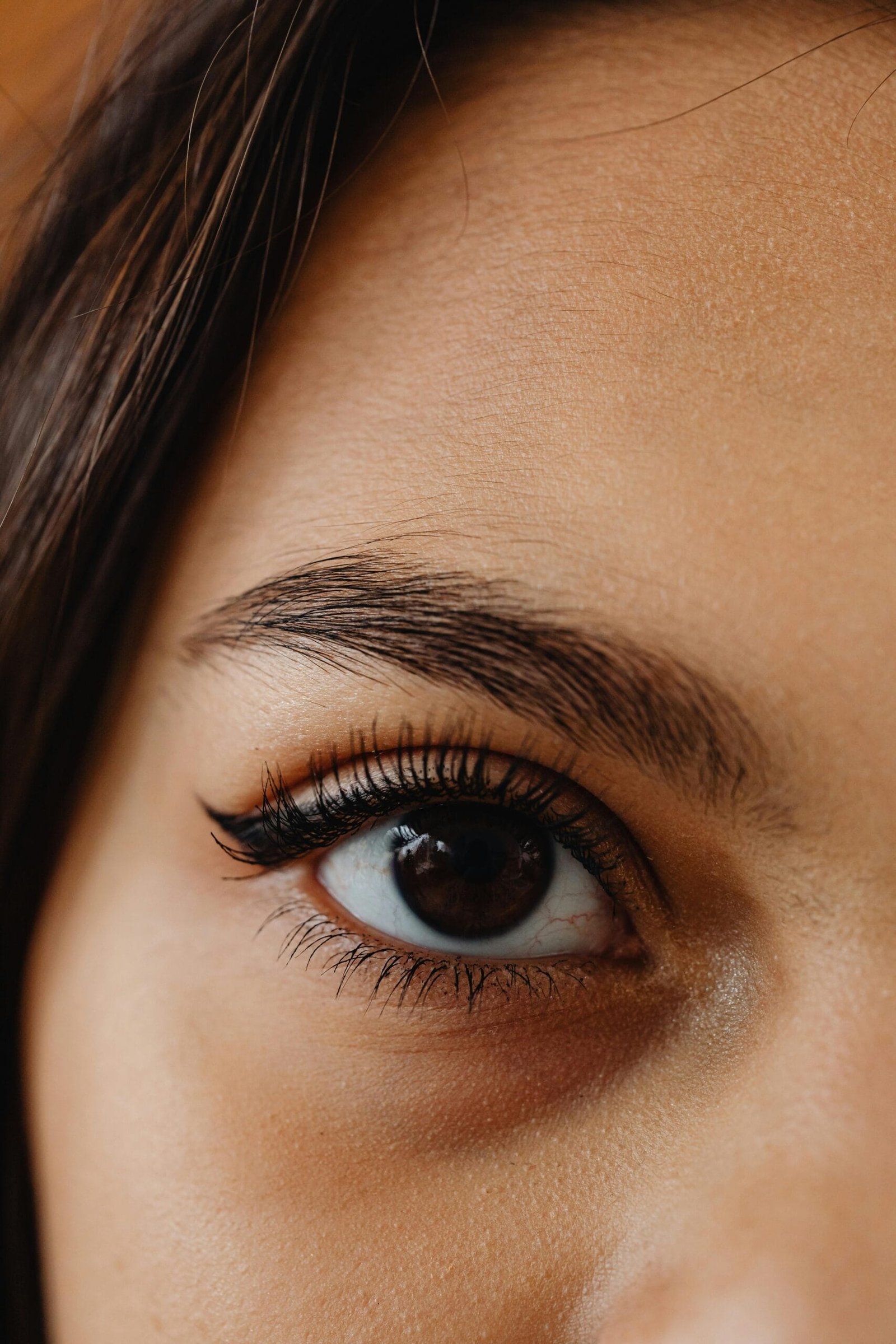 Primer plano de un ojo femenino con delineado negro estilo cat eye, pestañas largas y rizadas con rímel, ceja perfectamente definida y piel de rostro suave y bien cuidada. Maquillaje natural, enfoque en el cuidado de las cejas y maquillaje de ojos. Imagen ideal para blogs de belleza, tutoriales de maquillaje, tips para resaltar la mirada y rutinas de skincare facial.
