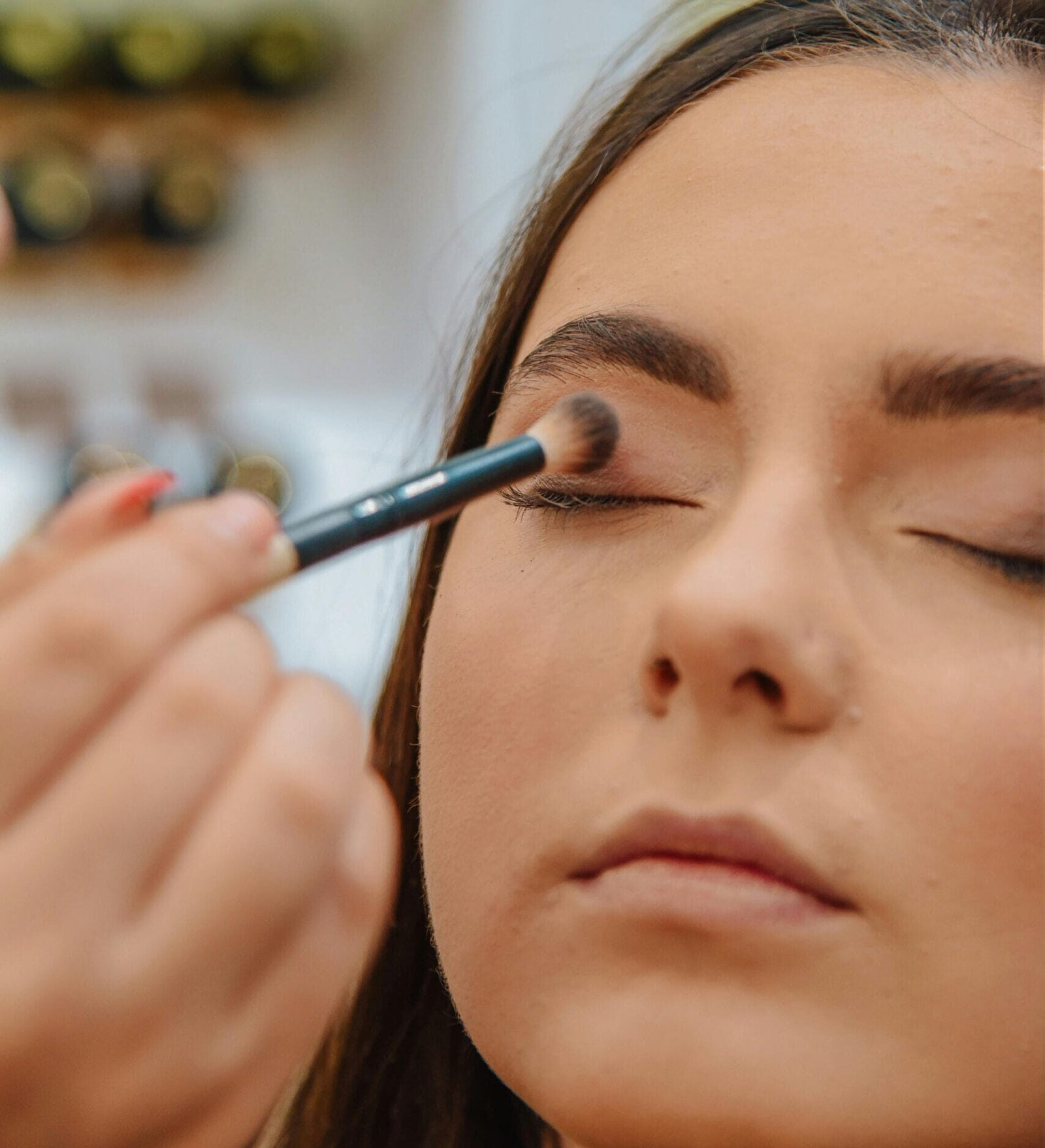 Mujer con rostro relajado y cejas perfectas, siendo maquillada con una brocha de maquillaje suave y sombras en tono rosa natural creando un maquillaje de diario. El maquillaje se está difuminando con precisión para lograr un acabado suave y uniforme,